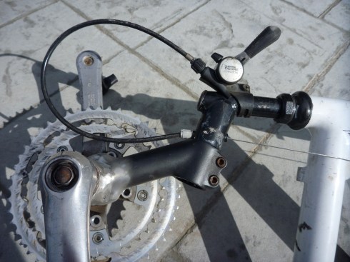 Shifter for the de-railer was re-attached to the bicycle neck. Shifter cable was run through the old brake cable housing. The use of two different bicycle necks bolted to together created the necessary crankshaft angle. Crankshaft housing was welded to the second bicycle neck.
